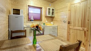A compact kitchen with wooden walls, a microwave, a refrigerator, a window with blinds, and a small cabinet. - Holiday home located near the sea; ideal for relaxing with family. (Mielno)