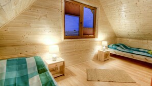 A cozy, wooden-paneled room with a bed, a nightstand, a lamp, and a window with shutters. - Holiday home located near the sea; ideal for relaxing with family. (Mielno)