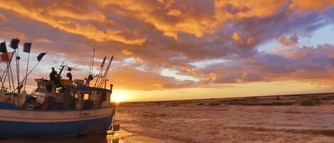 Ein Boot am Strand, im Hintergrund ein Sonnenuntergang.