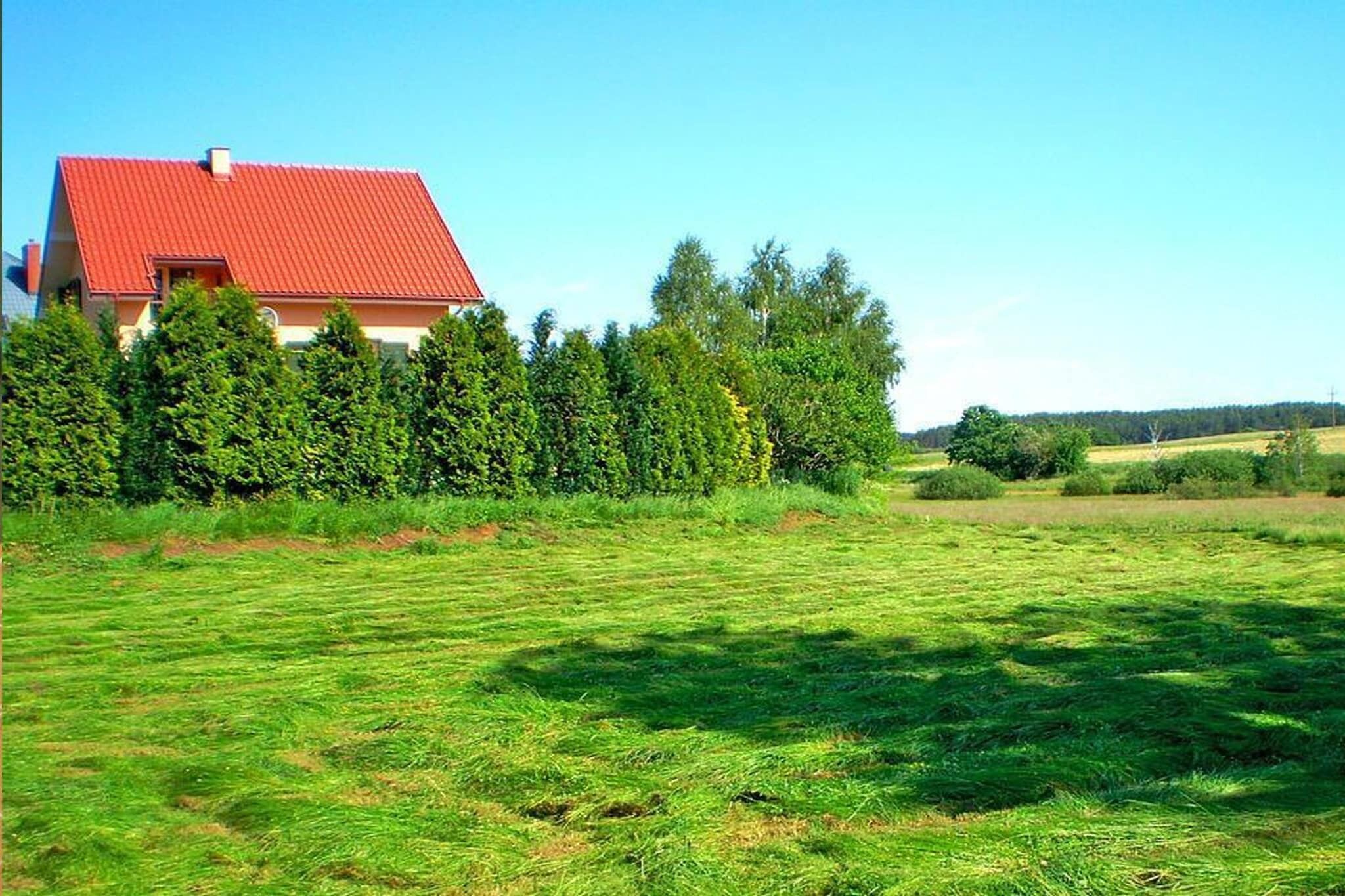 Ein Haus mit rotem Dach, umgeben von einem gepflegten Rasen und dichten Bäumen.