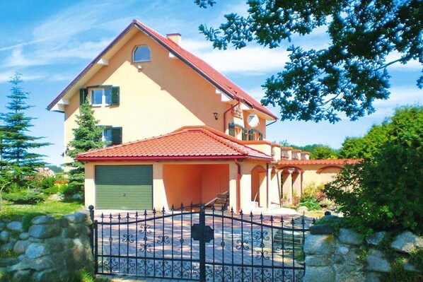 Una casa de dos pisos con techo de tejas rojas, un garaje y un muro de piedra al frente.