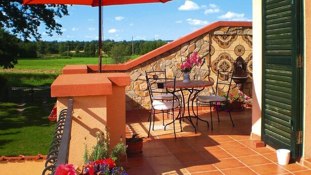 Eine Terrasse im Freien mit Tisch, Stühlen, einem roten Sonnenschirm und Topfpflanzen.