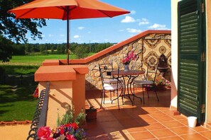 Un patio al aire libre con una mesa, sillas, un paraguas rojo y plantas en macetas.