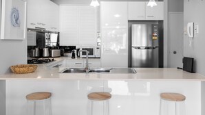 A modern kitchen with white cabinets, stainless steel appliances, a large island with stools, and pendant lighting. - Water Views with a Splash of Luxury (BONGAREE)
