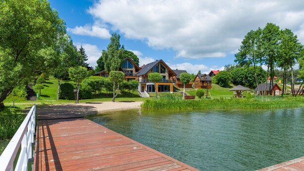 En træbrygge der fører ud til en sø med huse i baggrunden.