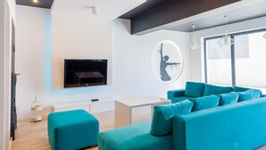 En moderne stue med en turkis sofa, et fladskærms-tv og et minimalistisk design.