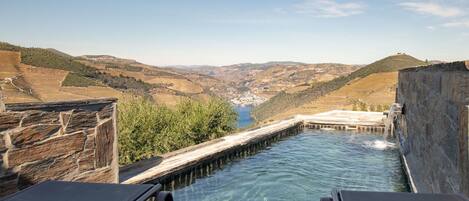 Piscina con muros de piedra y vista a un valle.