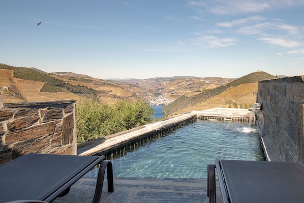 Piscina con muros de piedra y vista a un valle.