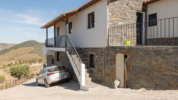 Ein zweistöckiges Haus mit einer Steinfassade und einem Balkon, vor dem ein Auto geparkt ist.