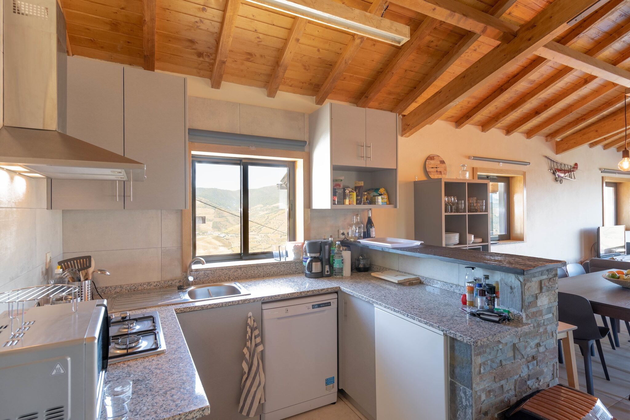 A modern kitchen with granite countertops, a dishwasher, and a large window offering a view of the countryside.