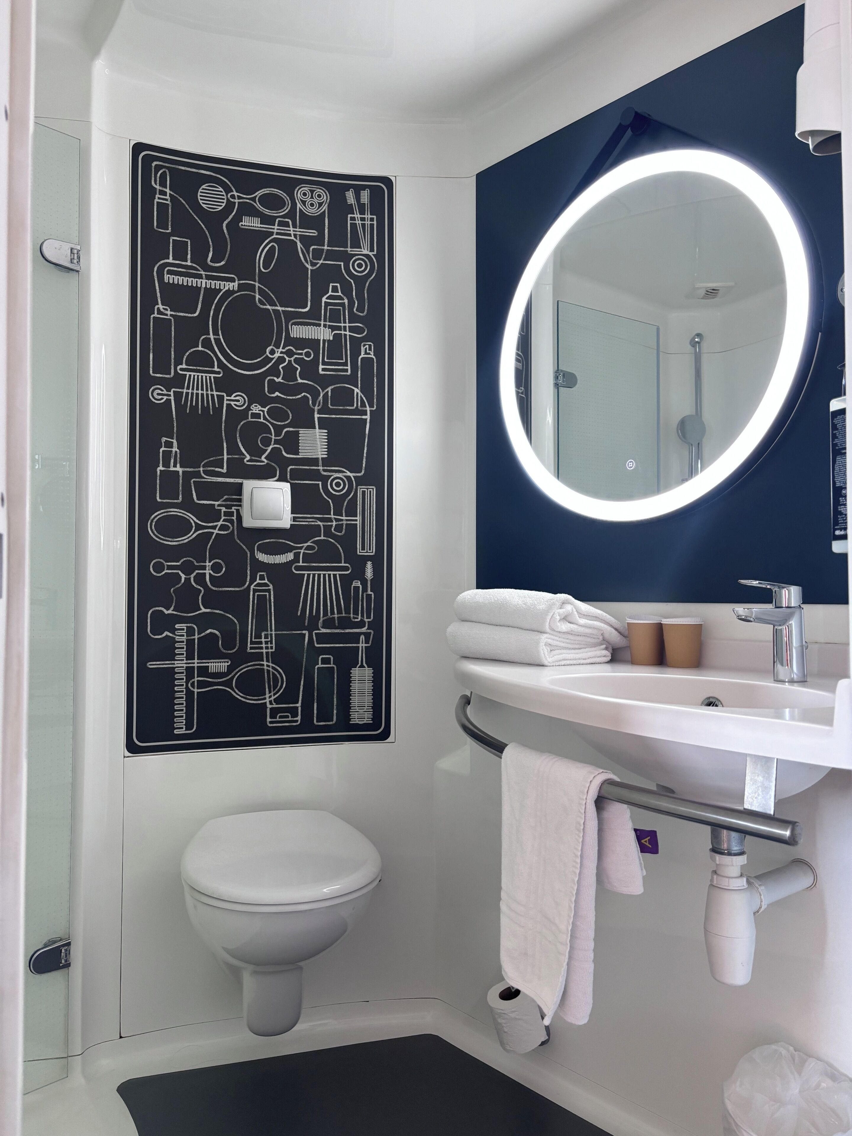 Un baño con inodoro, lavamanos con espejo y un cartel en la pared con símbolos de baño.