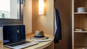 A modern room with a wooden desk, a laptop, a hat, and a jacket hanging on the wall. - Hôtel Ibis Cannes Mouans Sartoux (Mouans-Sartoux)