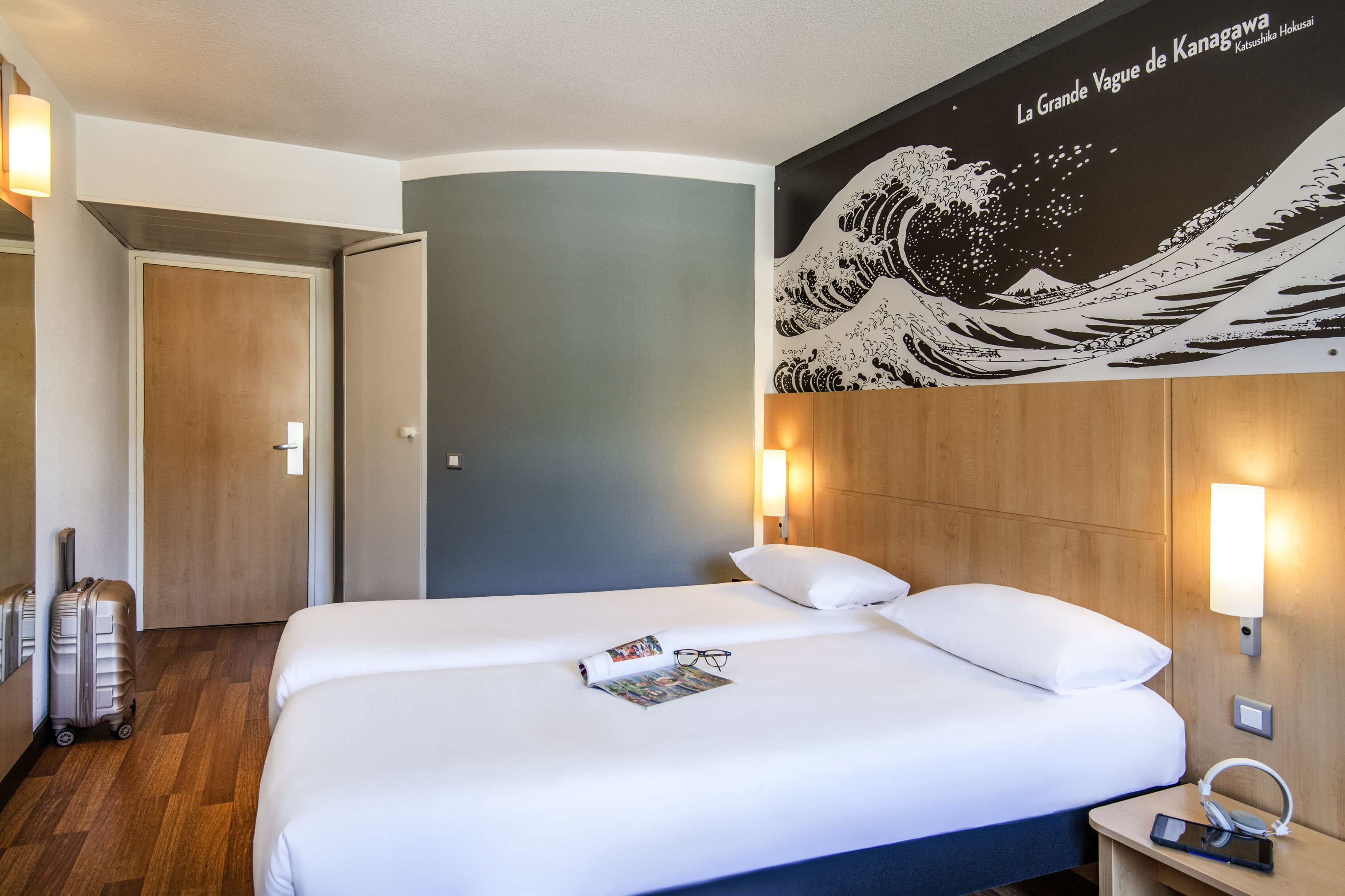 Een hotelkamer met een bed, een wandlamp, een nachtkastje en een wanddecoratie waarop een golf afgebeeld is.