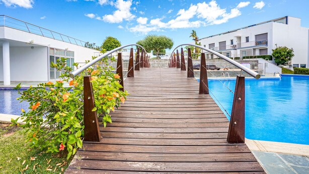 Una terraza de madera que conduce a una piscina con edificios modernos a ambos lados.