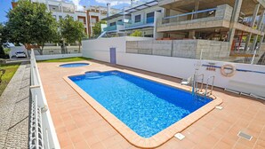 Une piscine rectangulaire, bordée d’une terrasse carrelée et entourée d’un mur blanc et d’une clôture en métal.