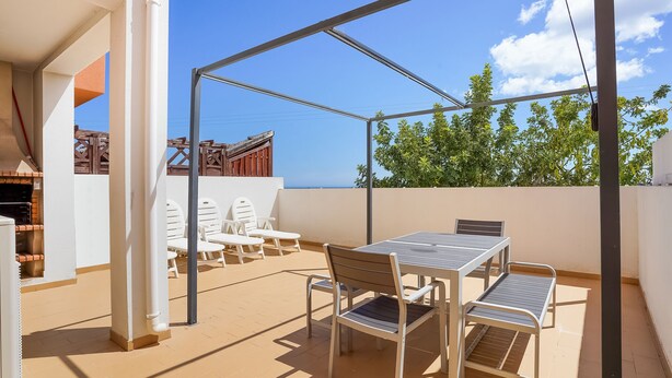 Une terrasse extérieure avec une table et des chaises, une pergola et une vue sur des arbres et un bâtiment en arrière-plan.