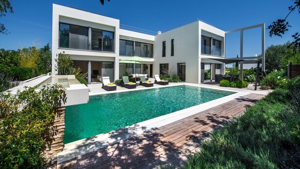 A modern two-story house with a swimming pool, outdoor seating, and lush greenery.