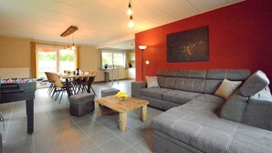A living room with a grey sofa, a wooden coffee table, a foosball table, and a dining area with chairs and a table. - Villa in Berismenil near Forest (Berismenil (La Roche-en-Ardenne) Ardennes)