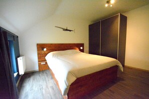 Een slaapkamer met een houten hoofdeinde, een bed met een witte dekbedovertrek, een garderobe en een aan de muur bevestigde decoratie van een vliegtuig.