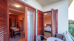 A balcony with a table and chairs, a sliding glass door leading to a room with a bed, and a view of greenery. - Lovely Apartment  in Biograd na Moru with Balcony (Biograd na Moru)