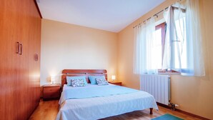 A bedroom with a wooden wardrobe, a bed with a white bedspread, two bedside lamps, a window with sheer curtains, and a radiator. - Lovely Apartment  in Biograd na Moru with Balcony (Biograd na Moru)