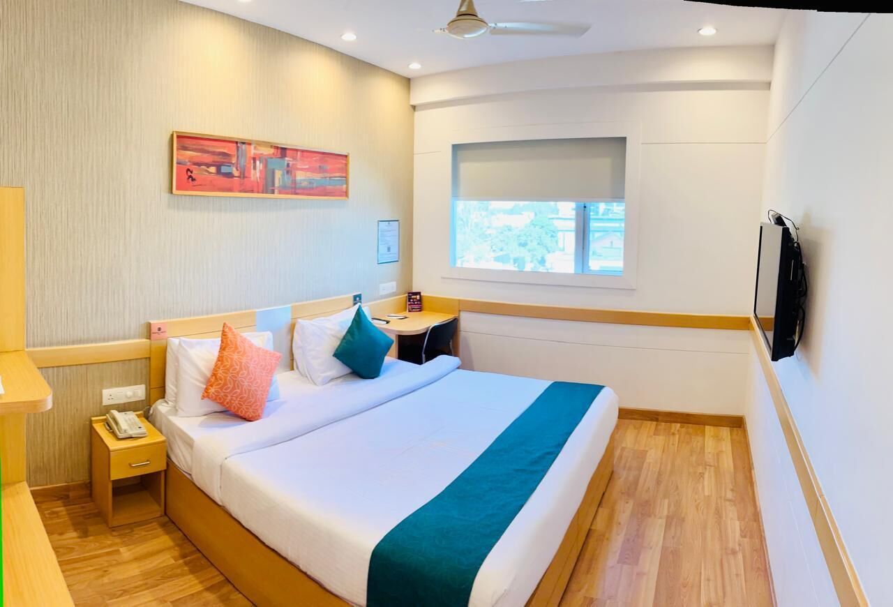 A hotel room with a bed, bedside table, nightstand, and a window with a view.