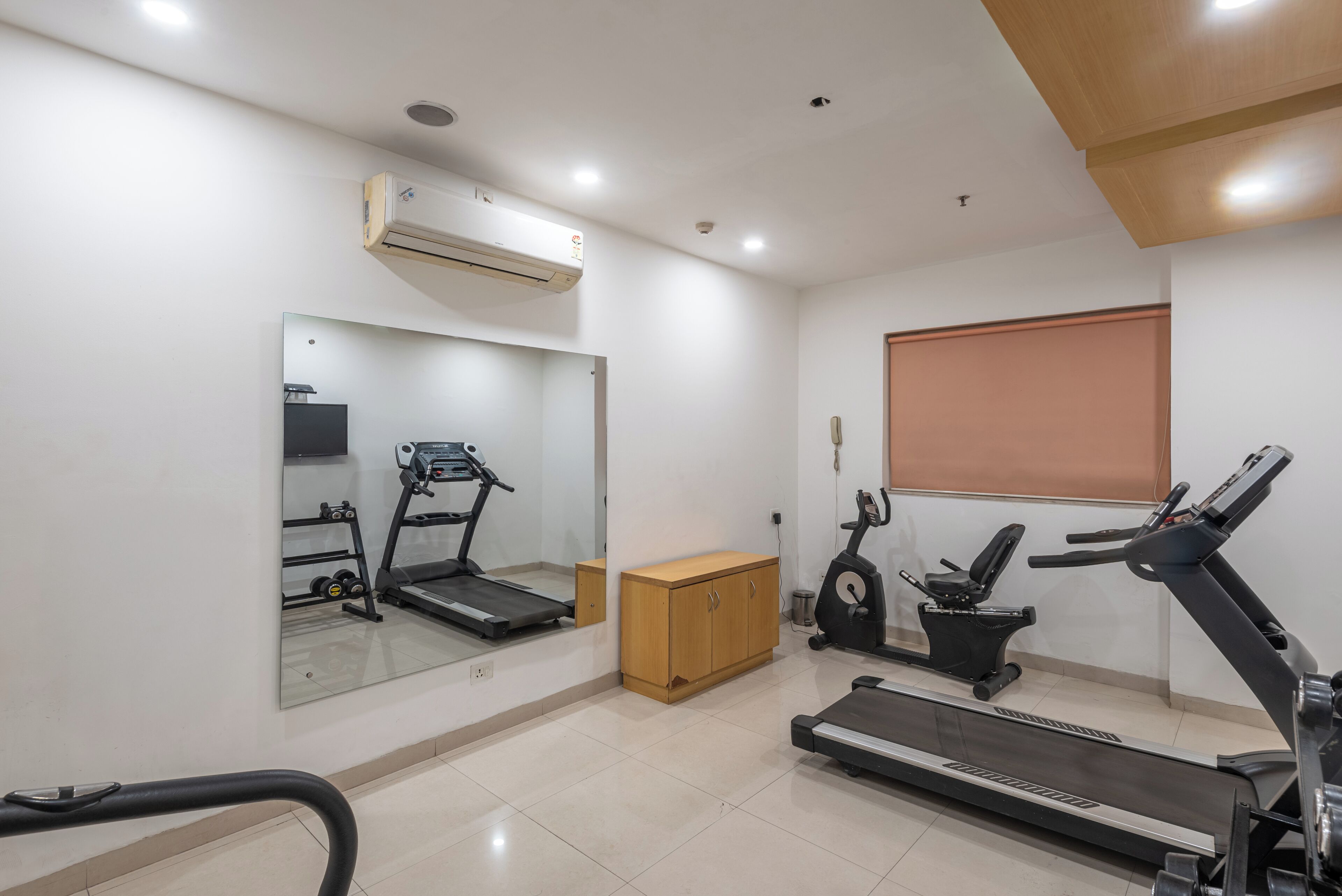 A gym with exercise equipment, a mirror, and a window with blinds.