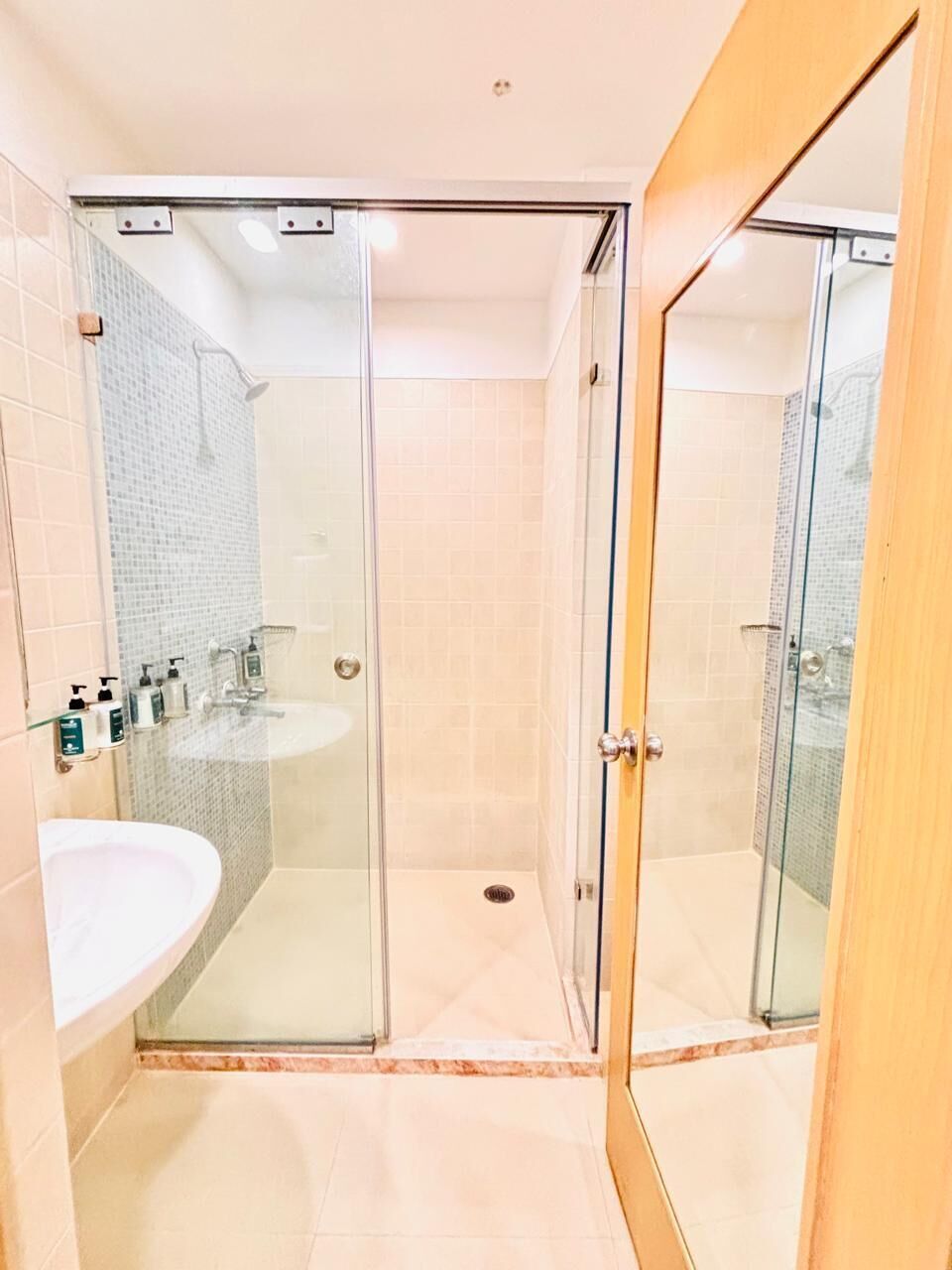 Un baño moderno con ducha envuelta en vidrio, lavamanos y espejo.