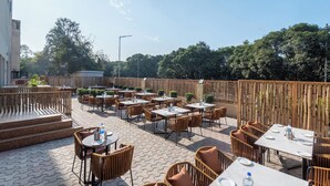 Un patio al aire libre con mesas y sillas, rodeado por una valla de madera y árboles.
