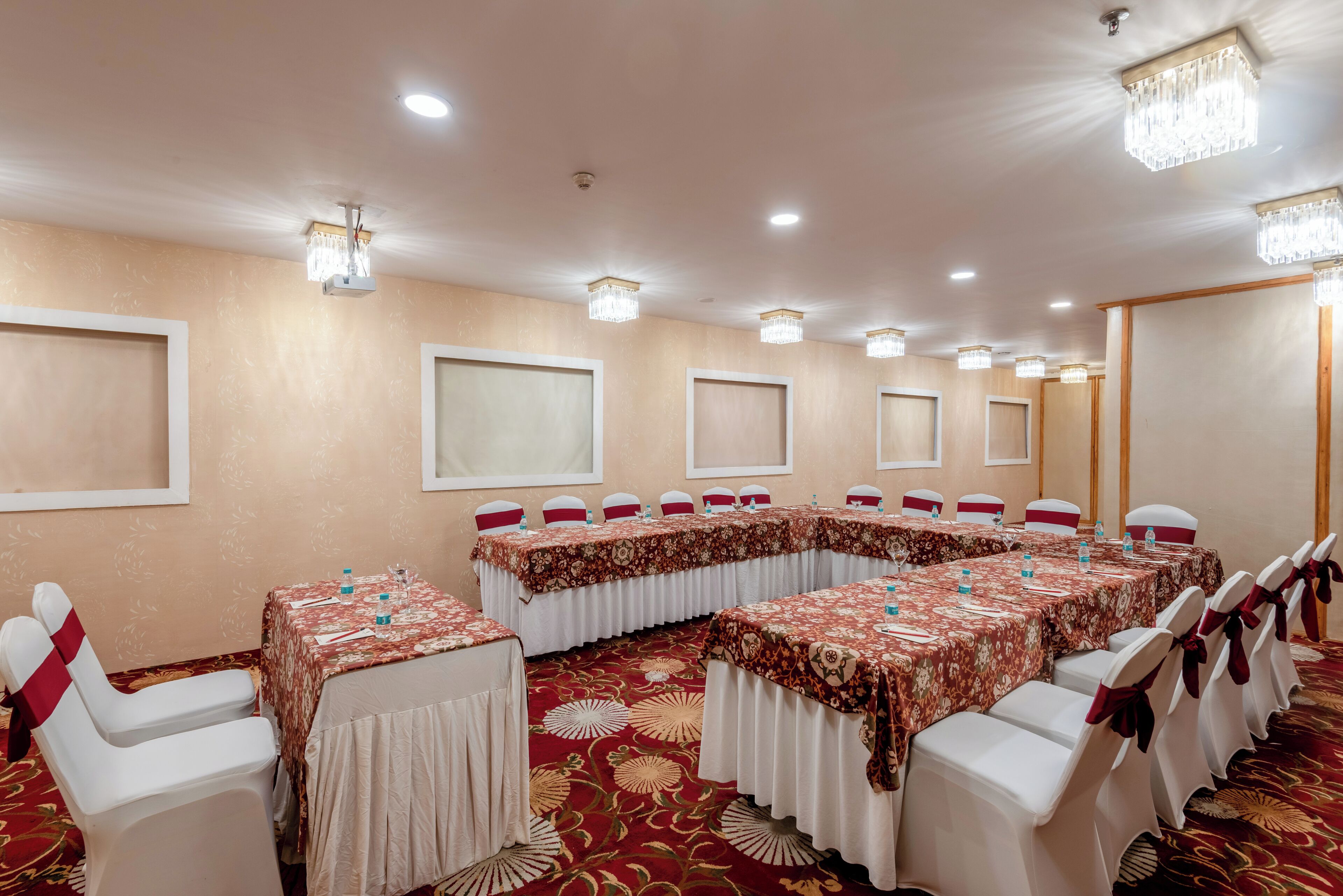 A conference room with long tables, white chairs, and chandeliers.