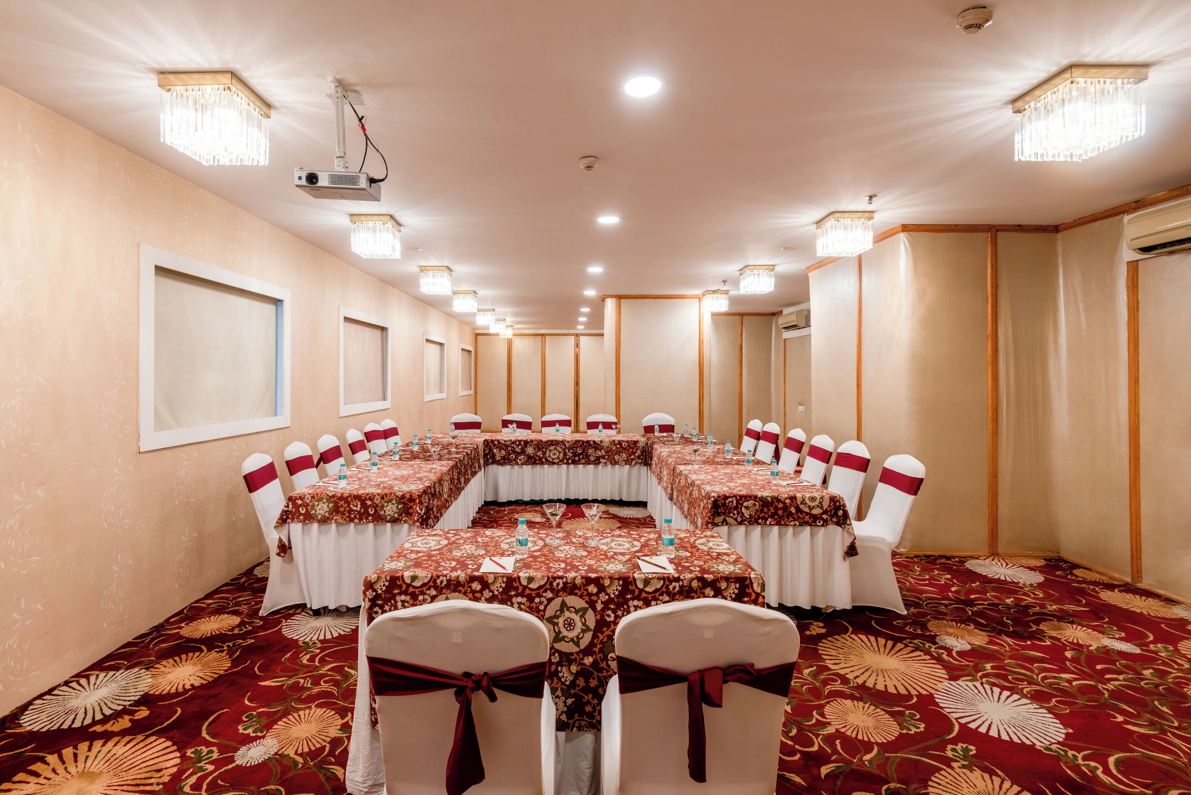 Un salón de conferencias con una larga mesa, sillas blancas y manteles con motivos florales rojos.