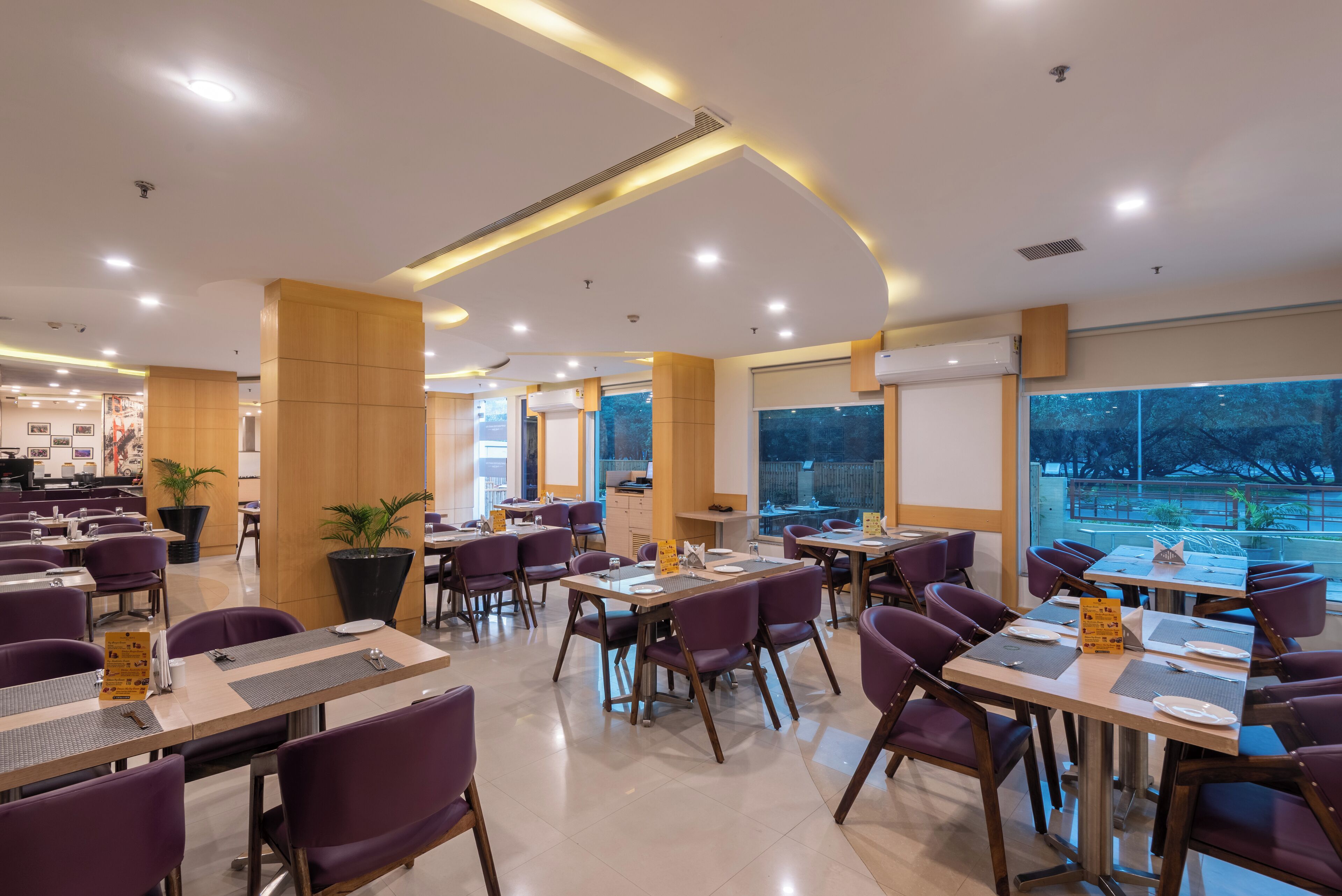 A modern restaurant with purple chairs, wooden tables, and a large window offering a view of the outdoors.