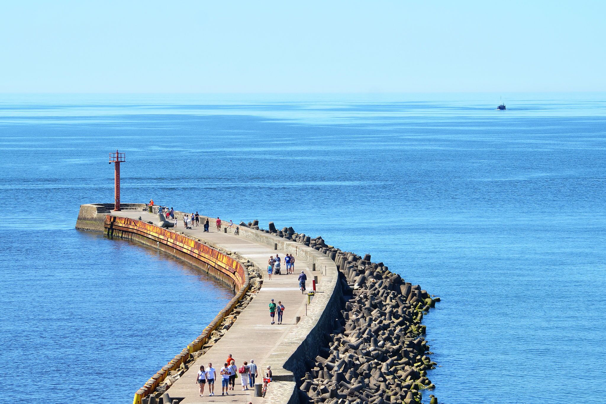 A pier extending into a calm sea with people walking along it.