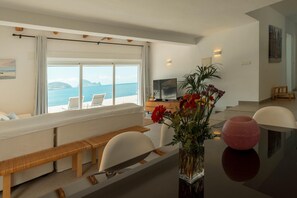 A modern living room with a large window, a sofa, a dining table, and a TV.