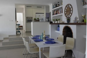 A modern dining area with a white table set for six, blue plates, and a fireplace with a clock above it.