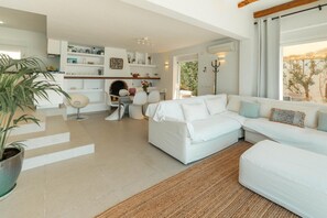 A modern living room with a white sofa, a dining area with a round table, and a kitchen with white cabinets.