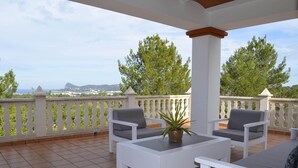 Eine Terrasse mit weißer Möbel, einem Blumentopf und Blick auf Bäume und eine entfernte Landschaft.