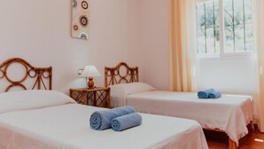 Ein Zimmer mit zwei Betten, einem Nachttisch, einer Lampe und einem Fenster mit Vorhängen.