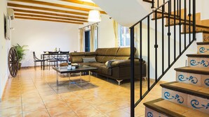 Un salon comprenant un canapé, une table basse et un coin repas. On y trouve également un escalier avec des marches décoratives.