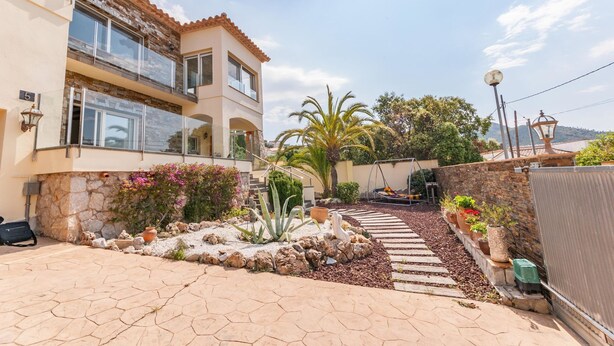 A two-story house with a stone facade, a paved patio, and a variety of plants and flowers. - Modern Villa near Beaches (Roses)