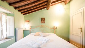 Ein ordentlich bezogenes Bett mit weißer Daunendecke und Kissen, ein Holz-Kopfbrett und ein kleiner Nachttisch mit einer Lampe.