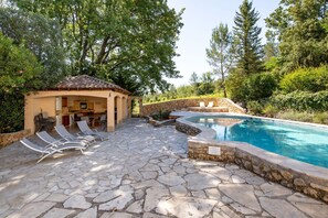 Una piscina de pedra amb gandules, un petit pavelló i una paret de pedra.