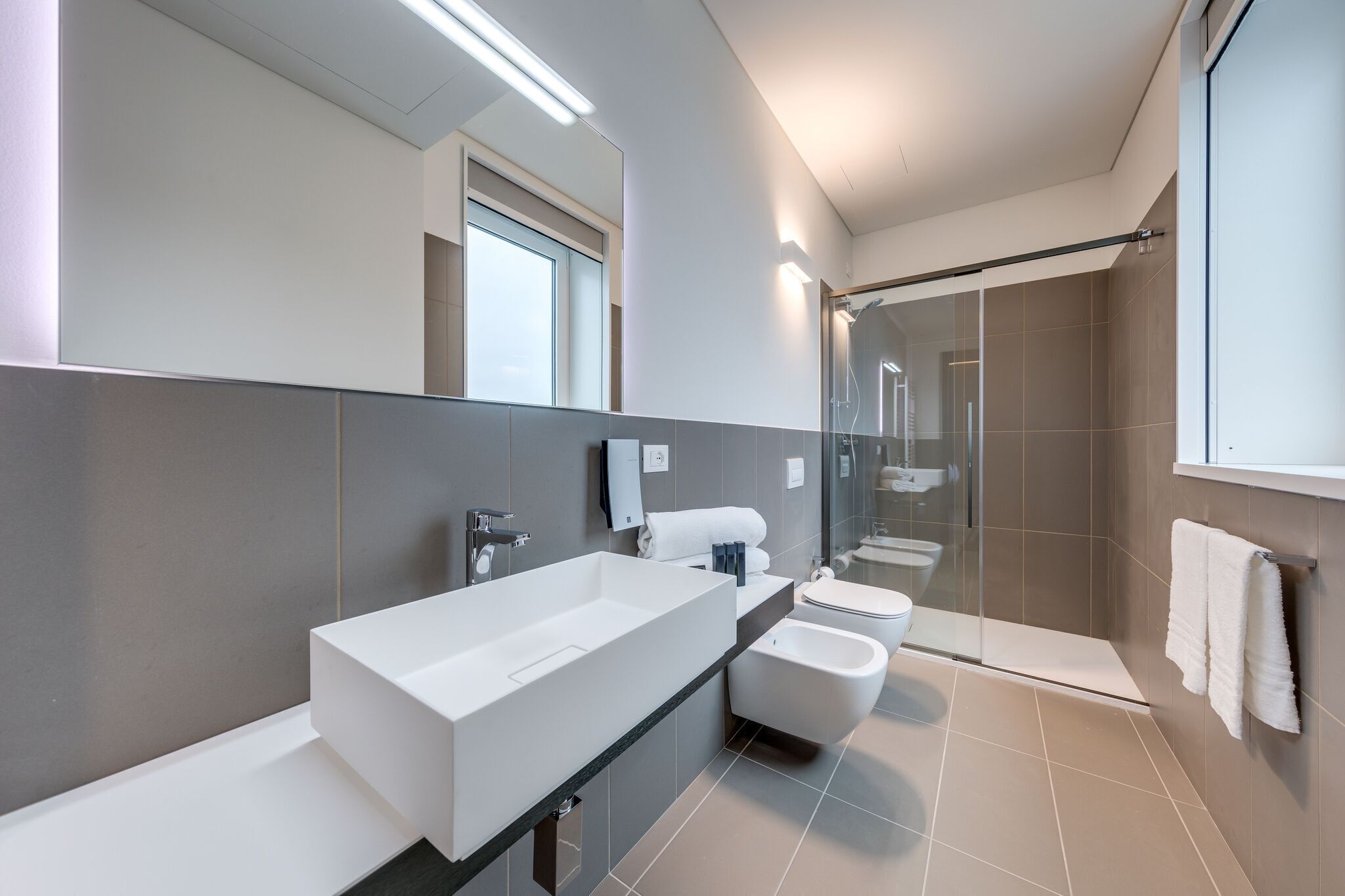 A modern bathroom with a large white sink, a toilet, and a shower area.