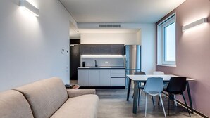 A modern kitchen with white cabinets and a stainless steel refrigerator. There is a dining area with a table and chairs.