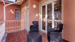 A balcony with two wicker chairs and a small table, a white railing, and a large window with curtains.