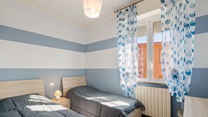 A bedroom with two beds, a window with curtains, a bedside lamp, and a radiator.