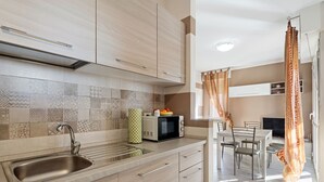 A modern kitchen with a stainless steel sink, a microwave, and a toaster. There is a dining area with a table and chairs.