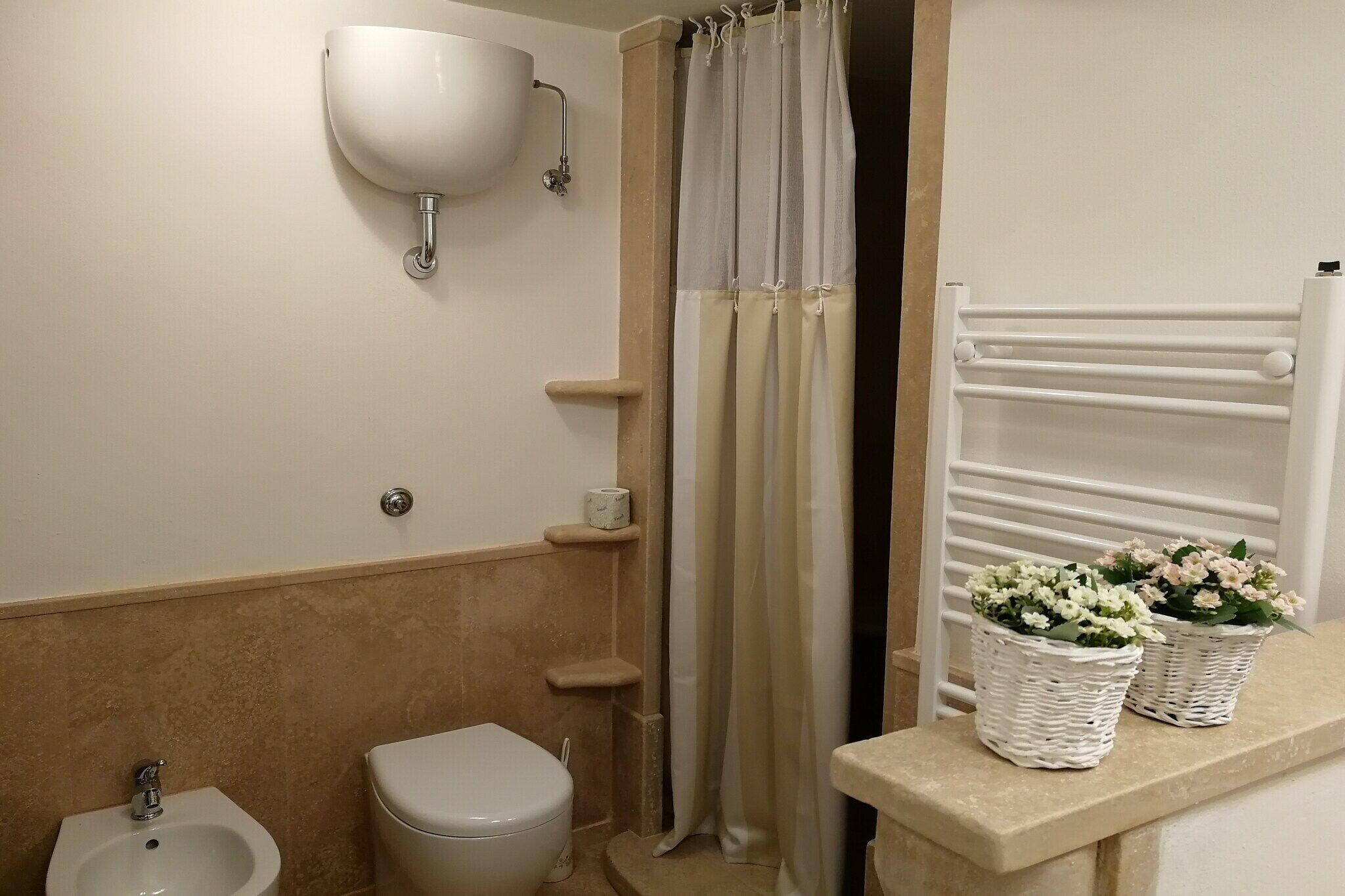 Un baño con inodoro, bidé, lavabo, cortina de ducha y dos cestas de mimbre con flores.