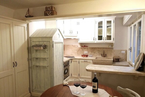 A kitchen with white cabinets, a wooden cabinet, a marble countertop, and a wine bottle.
