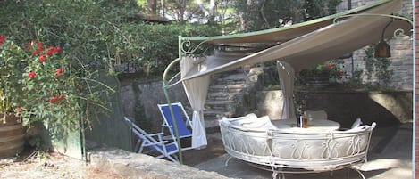 A boat docked near a stone wall, a covered seating area, and a chair with a white cover.